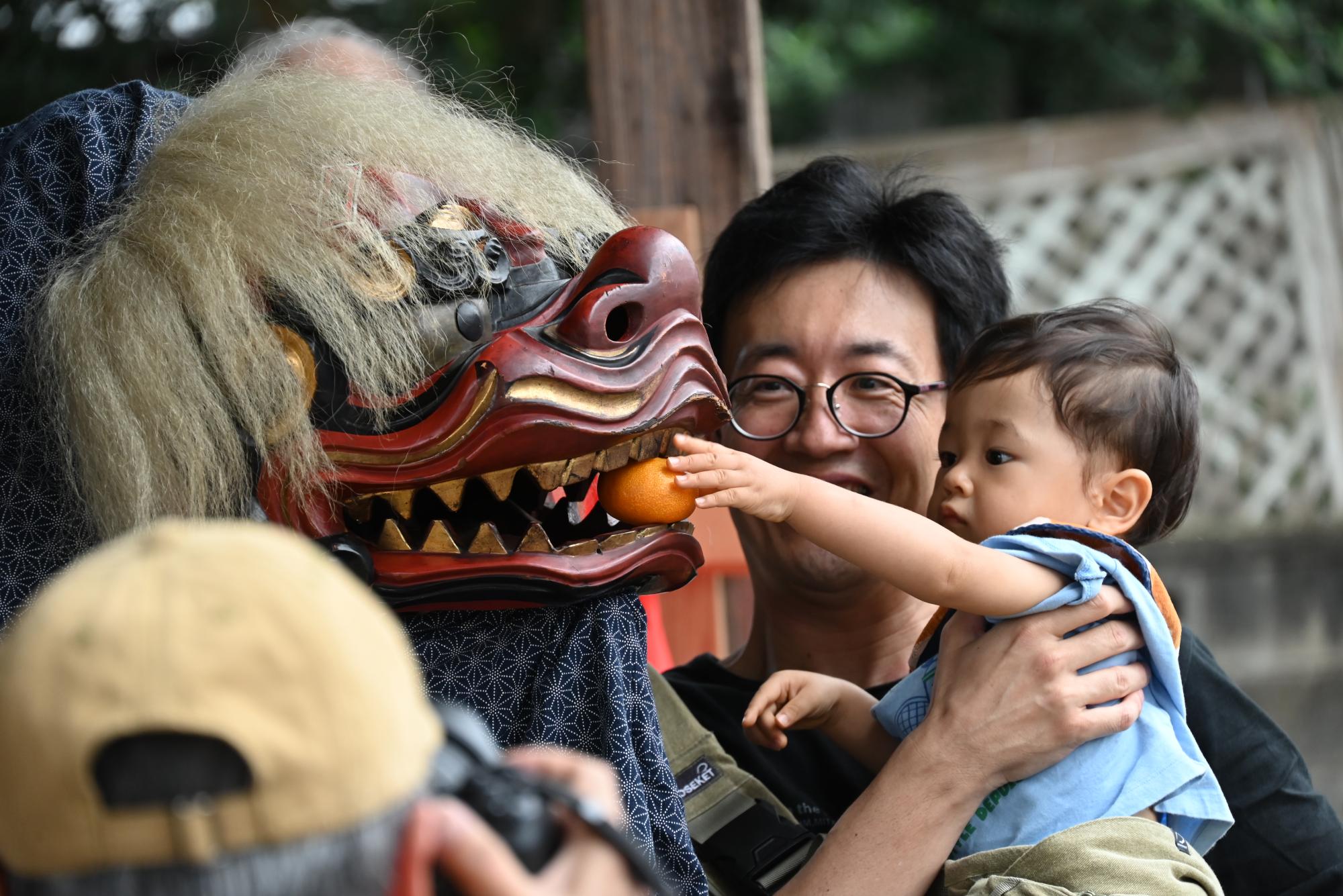 獅子舞に縁起物のみかんを与える観覧者