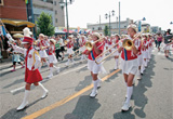 パレードで金管楽器を演奏しながら歩行者天国内を歩いている子どもたちの写真
